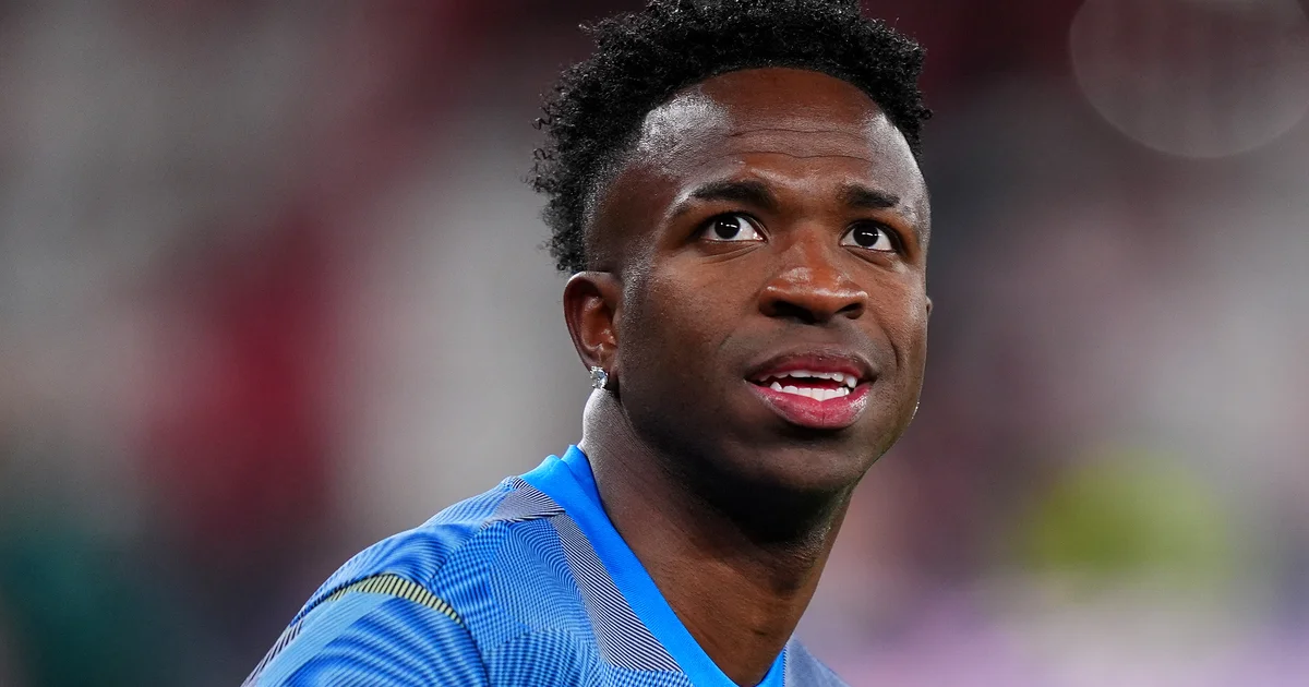 Ilustração de estádio com jogador negro cobrindo o ouvido, torcedores em sombras e balões de fala censurados, racismo e investigação UEFA