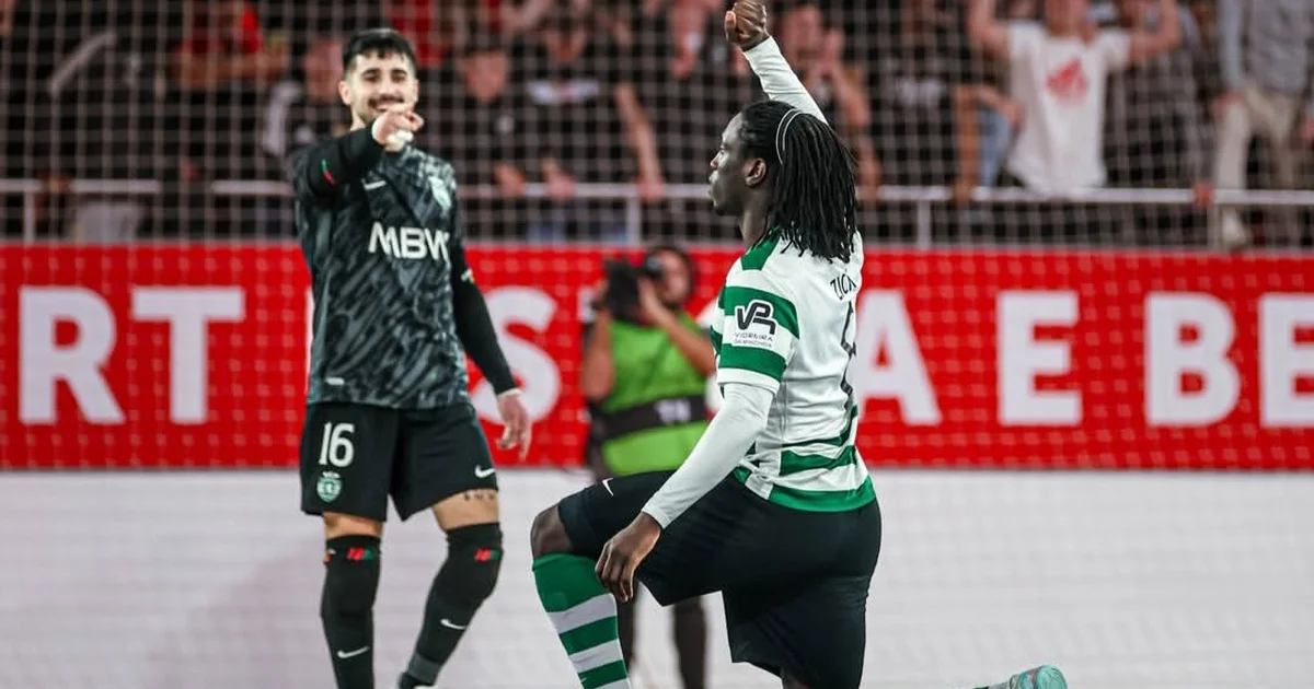Jogador de futsal ajoelhado com punho cerrado em gesto antirracista, quadra polida e torcida ao fundo.