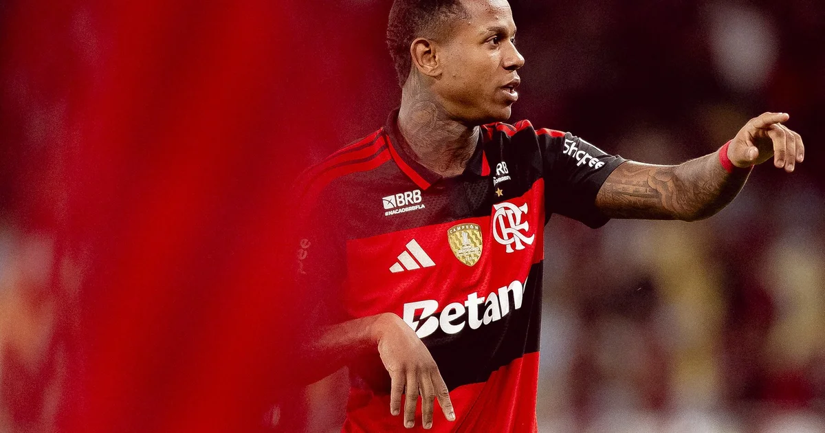 Silhueta de atacante do Flamengo afastado, sem rosto, com mala na beira do campo enquanto ônibus do time parte sob as luzes do estádio
